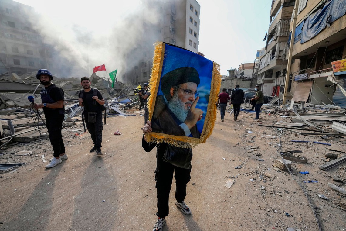 A woman holding a picture of the assassinated Hezbollah leader Hassan ­Nasrallah at the site of an Israeli air strike, Dahiyeh, Beirut